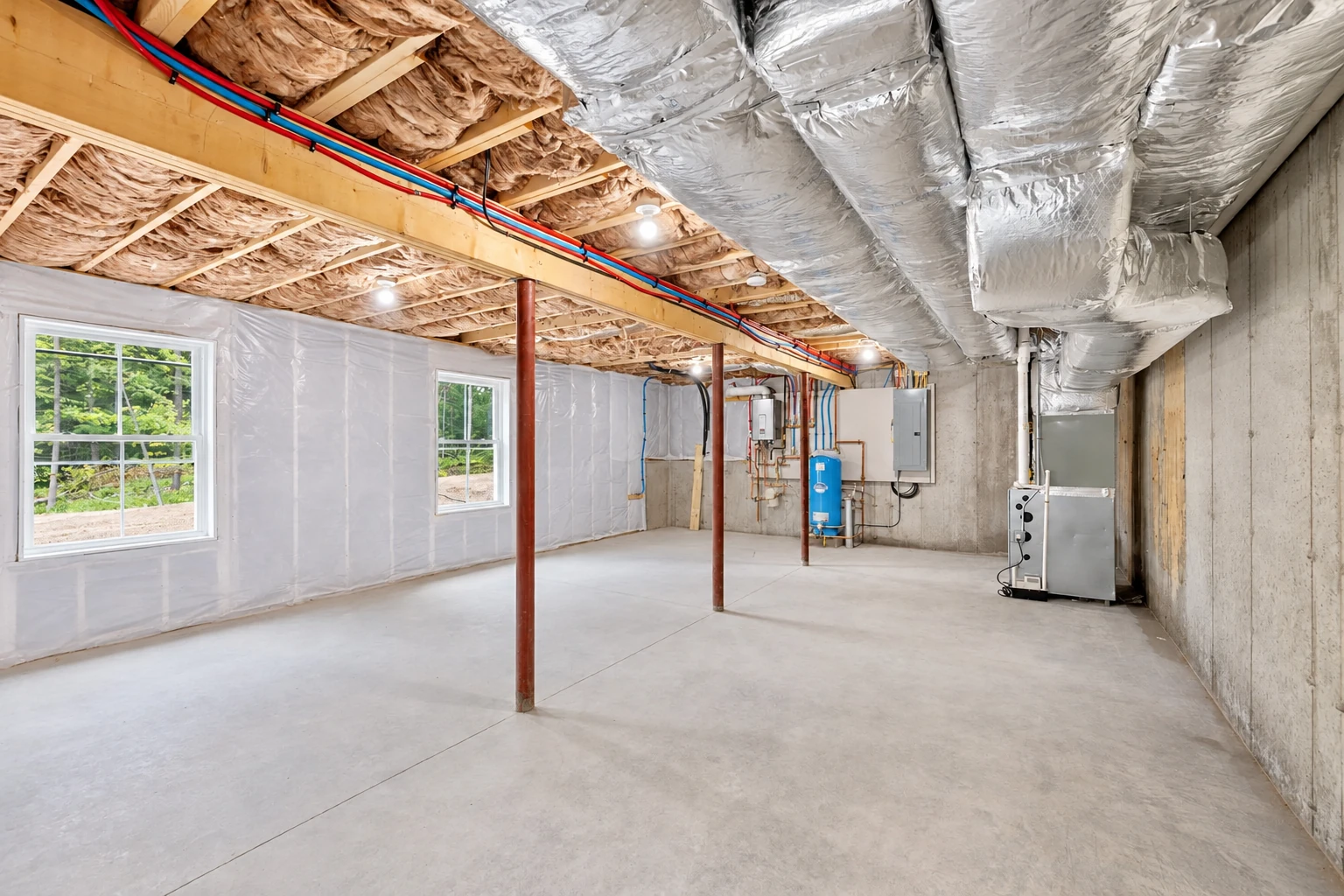 Basement with fiberglass insulation between ceiling joists, plastic-covered walls, and large silver HVAC ducts overhead.
