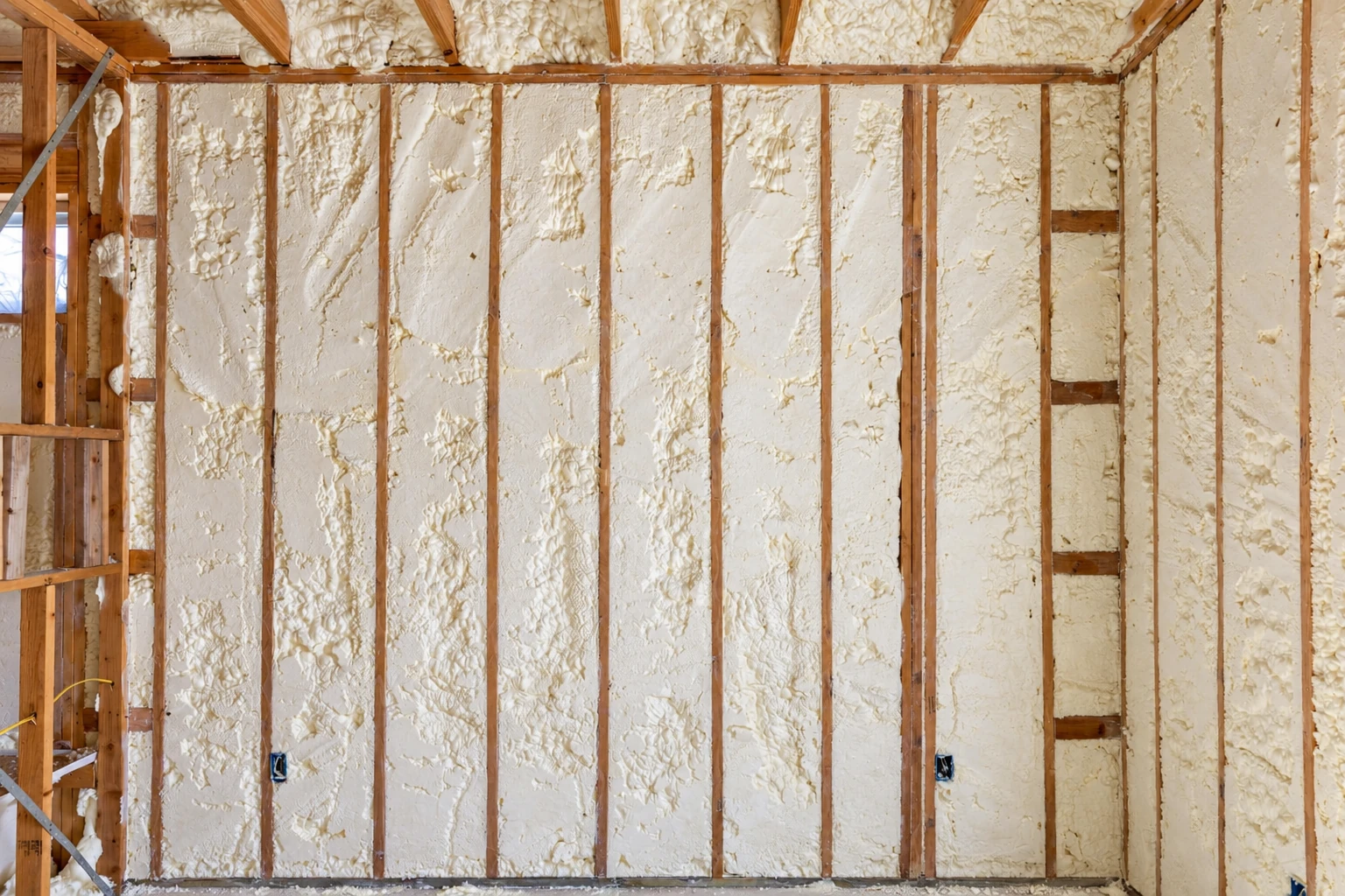 Exposed wall studs and ceiling are filled with rough, pale closed-cell spray foam insulation.