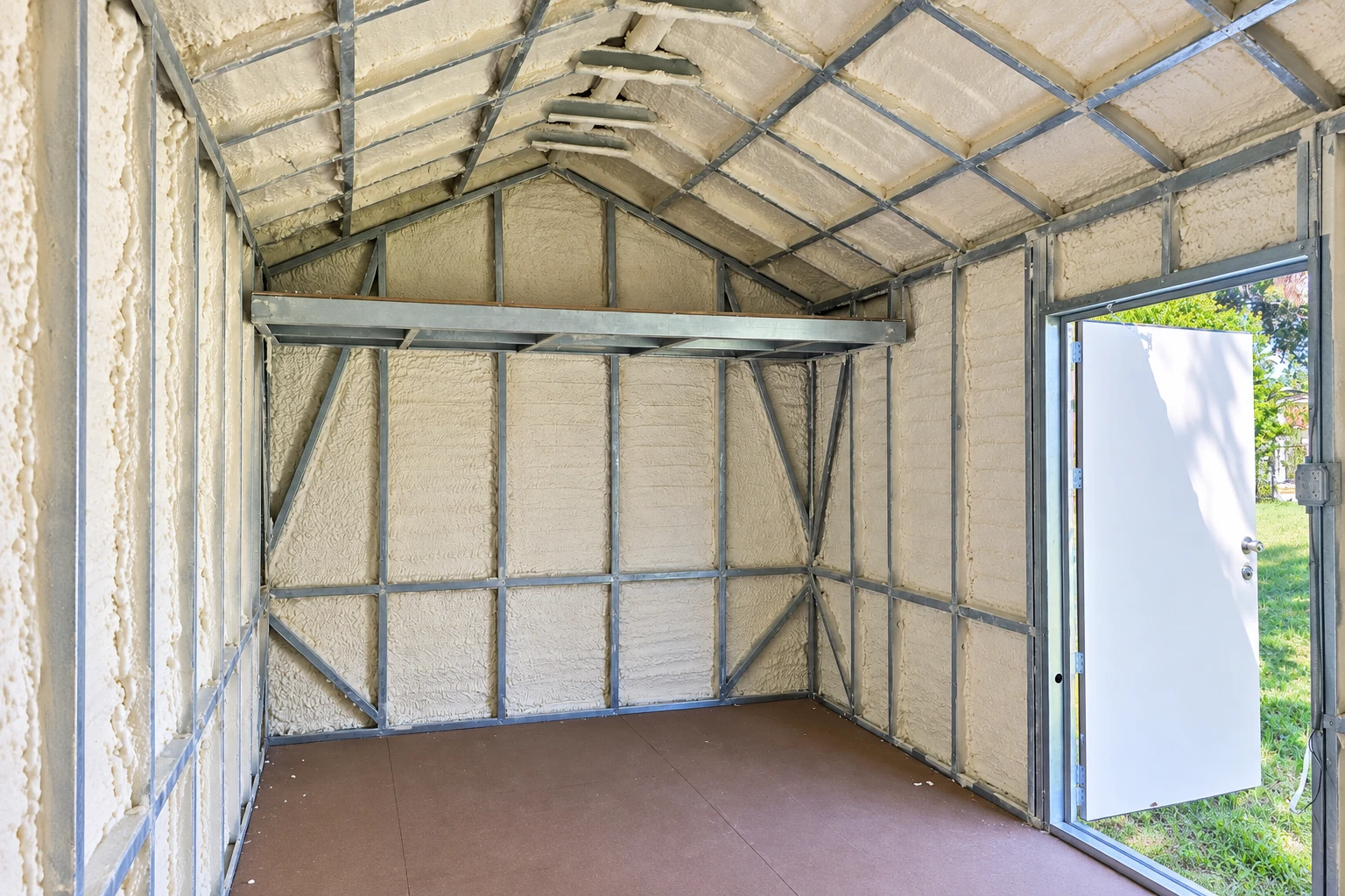 Spray foam insulation covers the walls and pitched ceiling of a metal-framed commercial room.