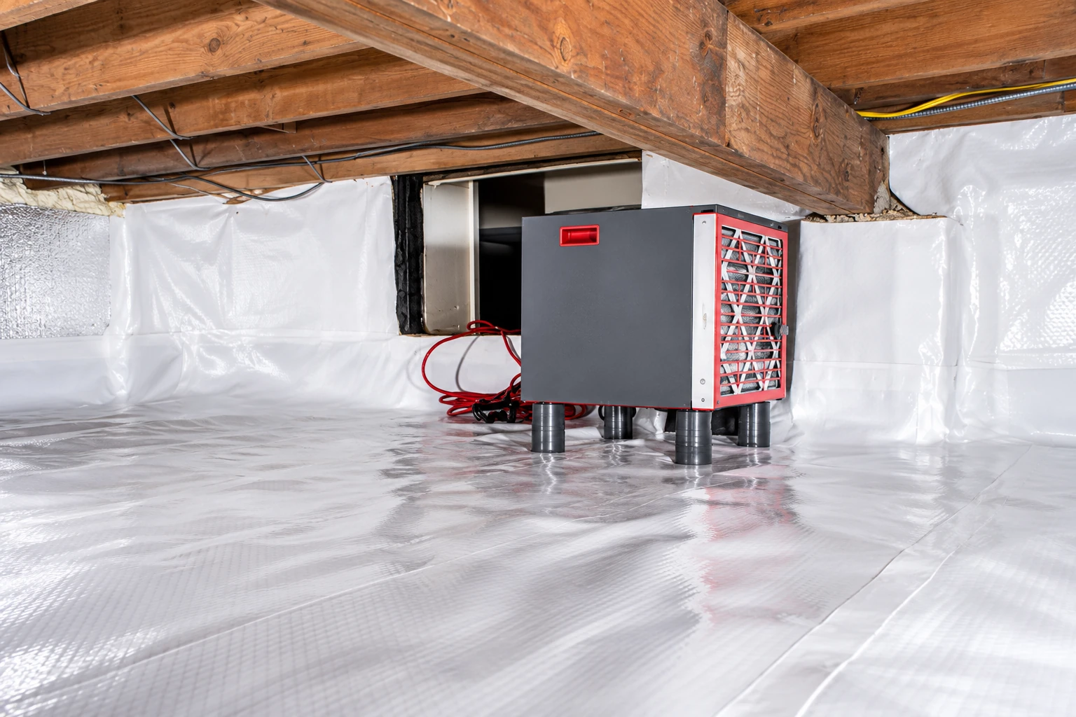 Crawl space with white plastic covering the floor and walls, exposed wooden joists, and a dehumidifier.