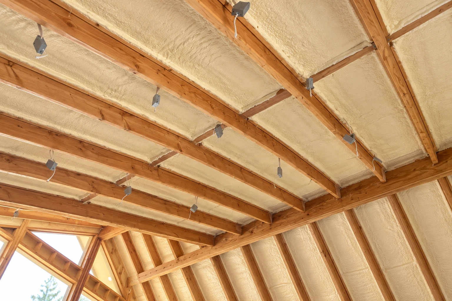 Open-cell spray foam fills the roof and wall cavities of a timber-framed building, with exposed beams and wiring.